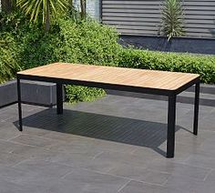 a wooden table sitting on top of a cement floor next to plants and bushes in front of a building