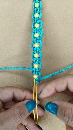 two hands are working on a piece of blue and yellow crocheted fabric with gold hooks