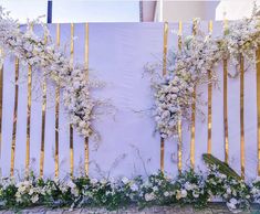 white flowers and greenery are arranged on the side of a wooden fence with gold bars