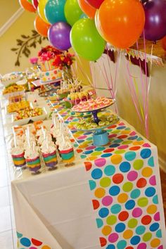 a table topped with lots of colorful balloons and cupcakes on top of it