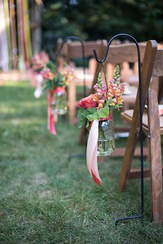 flowers in mason jars are hanging from the back of an outdoor ceremony set - up