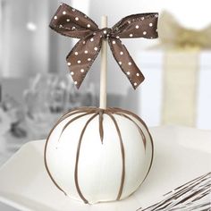 a white pumpkin decorated with brown polka dots and a bow on it's head