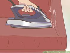 a person ironing clothes with an iron on the back of a red chair that is being held by a hand