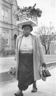 an old woman walking down the street carrying bags on her head