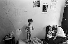 an old black and white photo of two people in a bedroom with a toddler standing on the bed