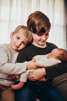 two young boys are sitting on a couch with their arms around each other as they hold a baby