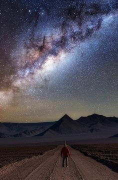 a man walking down a dirt road under a night sky filled with stars and the milky