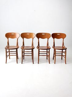 four wooden chairs are lined up against a white background with one chair facing the other