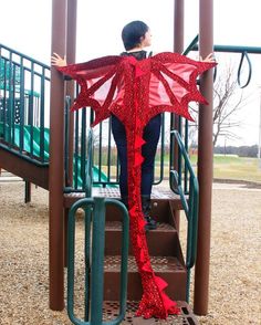 a woman standing on top of a slide next to a red dragon costume at a playground