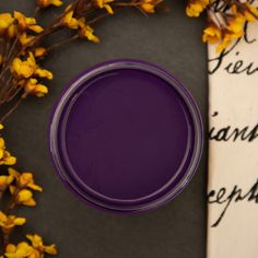 a purple paint in a glass bowl next to some yellow flowers and an old paper