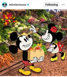 two mickey mouses are standing in front of a produce stand and pointing to each other