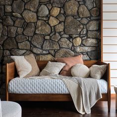 a bed sitting next to a stone wall with pillows on it's headboard