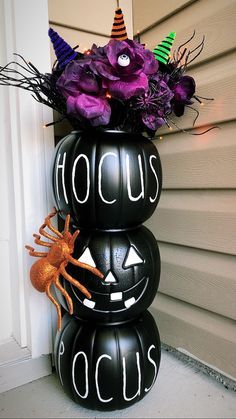 a halloween decoration made out of black pumpkins with purple flowers in the middle and a spider on top