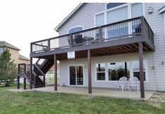 a house that has a deck and chairs in front of it on the grass outside