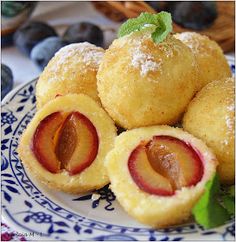 several pastries on a blue and white plate with fruit in the background, including plums