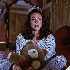 a woman wearing a tiara and holding a teddy bear in her lap, smiling at the camera