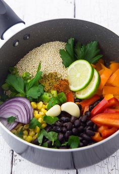 a pot filled with vegetables and rice on top of a white wooden table next to utensils