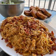 a white plate topped with pasta and meat next to a bowl of bread on a table