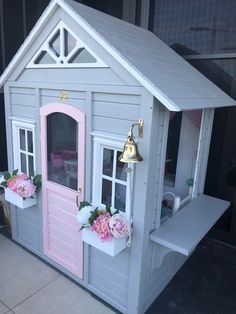 a doll house with pink doors and flowers on the window sill next to it