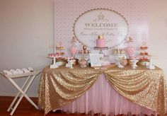 a table with pink and gold desserts on it's sides, along with a welcome sign