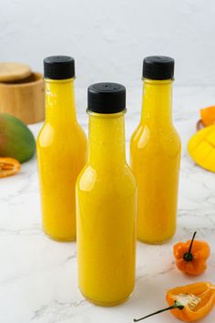 three bottles filled with yellow liquid sitting on top of a white marble counter next to sliced oranges