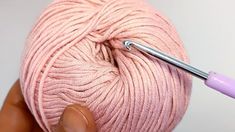 a ball of pink yarn with a crochet hook in the middle, being held by someone's hand