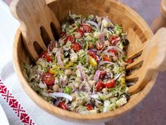 a salad in a wooden bowl with spoons and napkin on the table next to it