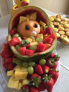 a watermelon cut in to look like a baby bear surrounded by fruits and pastries