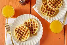 three waffles on white plates with orange juice