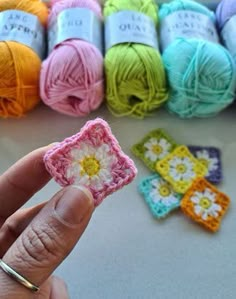 a hand holding a tiny crochet flower in front of several balls of yarn