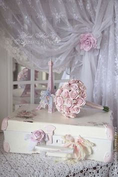 a white suitcase with pink flowers on top of it next to a lace covered window