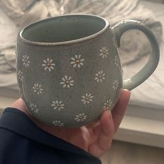 a hand holding a ceramic mug with daisies on it