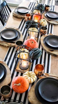 a table set with black plates and pumpkins