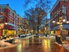 a city street is covered in snow and lit up with christmas lights on the buildings