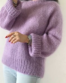 a woman is wearing a purple sweater and holding her hand up to her face while standing in front of a white wall