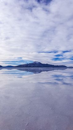 the sky is reflected in the still water at low tide beach, with mountains in the distance