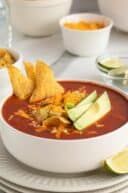 a bowl of chili soup with tortilla chips and avocado on the side