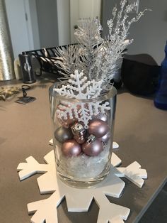 a glass vase filled with ornaments on top of a table next to snowflakes