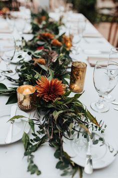 a long table is set with white plates and silverware, gold candlesticks and flowers