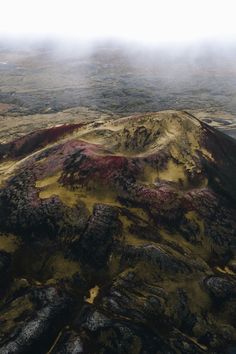 an aerial view of a mountain covered in red and yellow grass, with low lying clouds