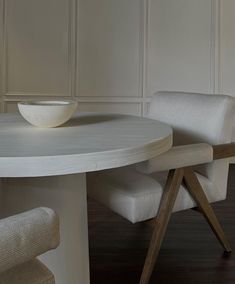 a bowl sitting on top of a white table next to two chairs and a bench