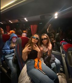 two women sitting in the back of a bus with their arms around each other and wearing sunglasses