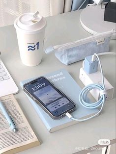 an open book and cell phone on a table next to a coffee cup with a pen