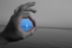 a person holding their hand out towards the ocean with a sailboat in the distance