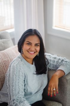 a woman sitting on top of a couch smiling at the camera with her hands in her pockets