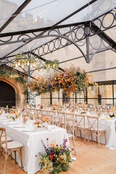 an indoor venue with tables and chairs covered in white linens, floral centerpieces and hanging chandeliers