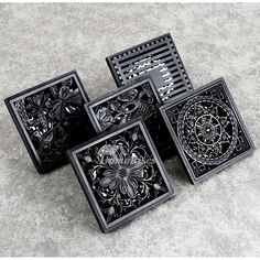 four black square trays with designs on them sitting next to each other in front of a concrete floor