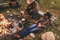 three people sitting around a campfire with drinks