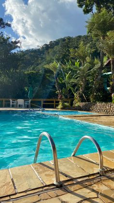 an empty swimming pool with chairs and trees in the background