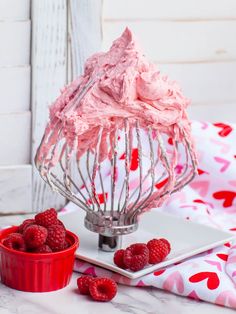 raspberry frosting in a wire whisk with fresh raspberries next to it